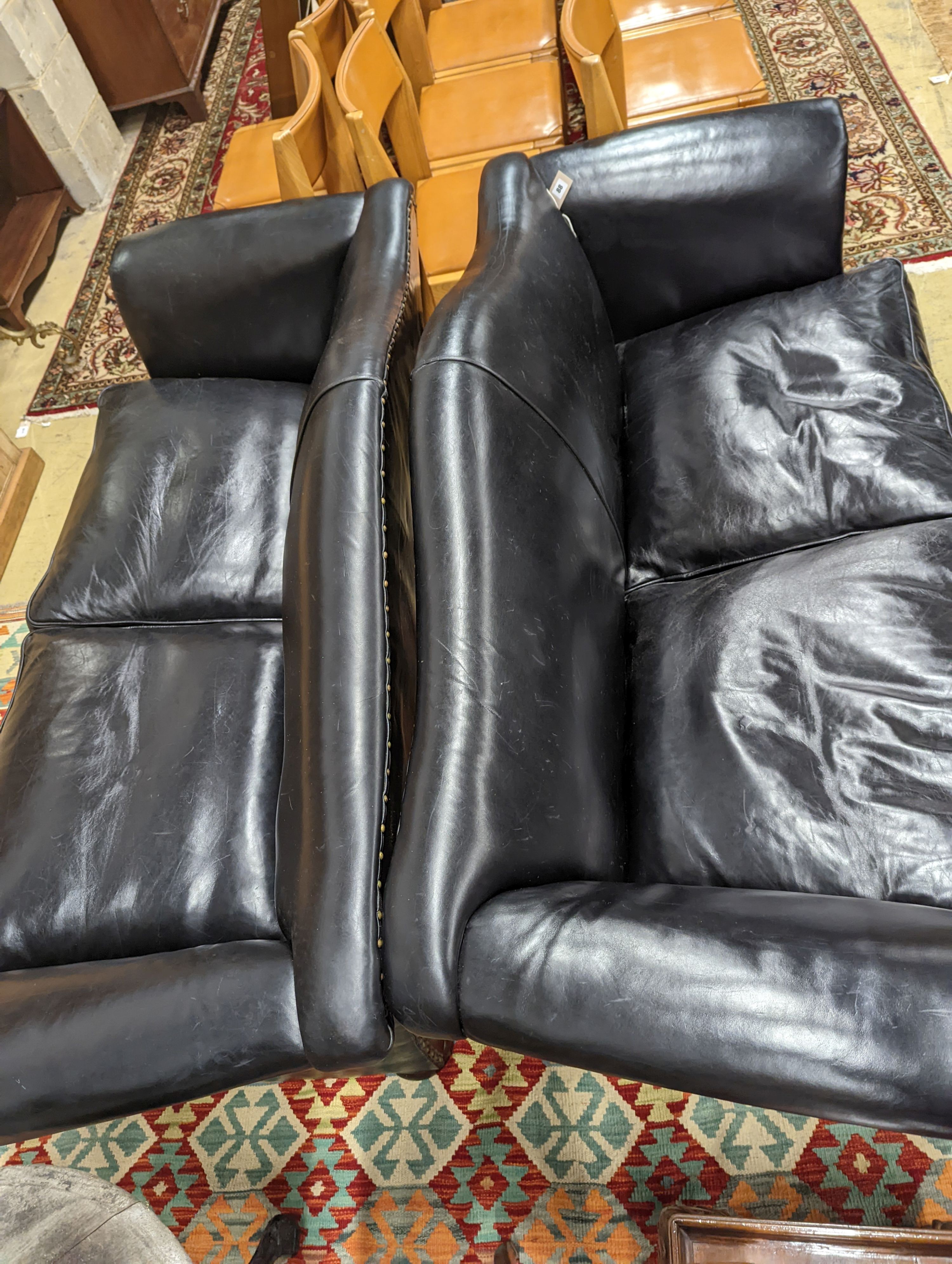 A pair of black leather scroll arm two seater settees on flat bun feet, length 184cm, depth 80cm, height 93cm